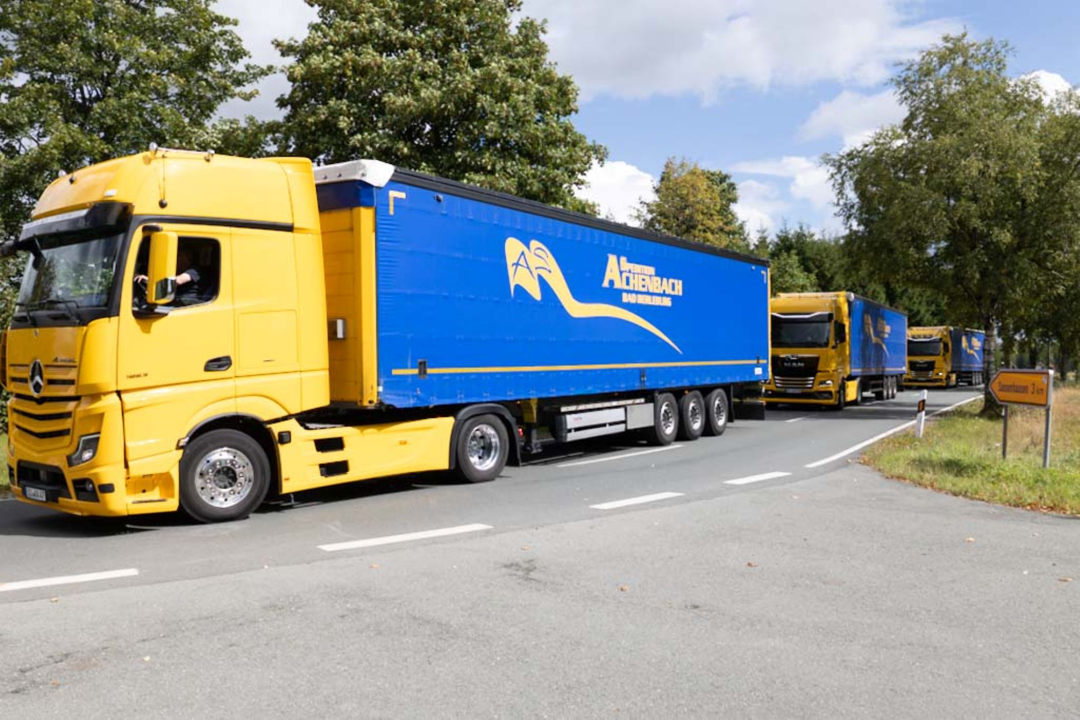 Gelber Lkw-Konvoi der Spedition Achenbach fährt auf Landstraße bei Bad Berleburg