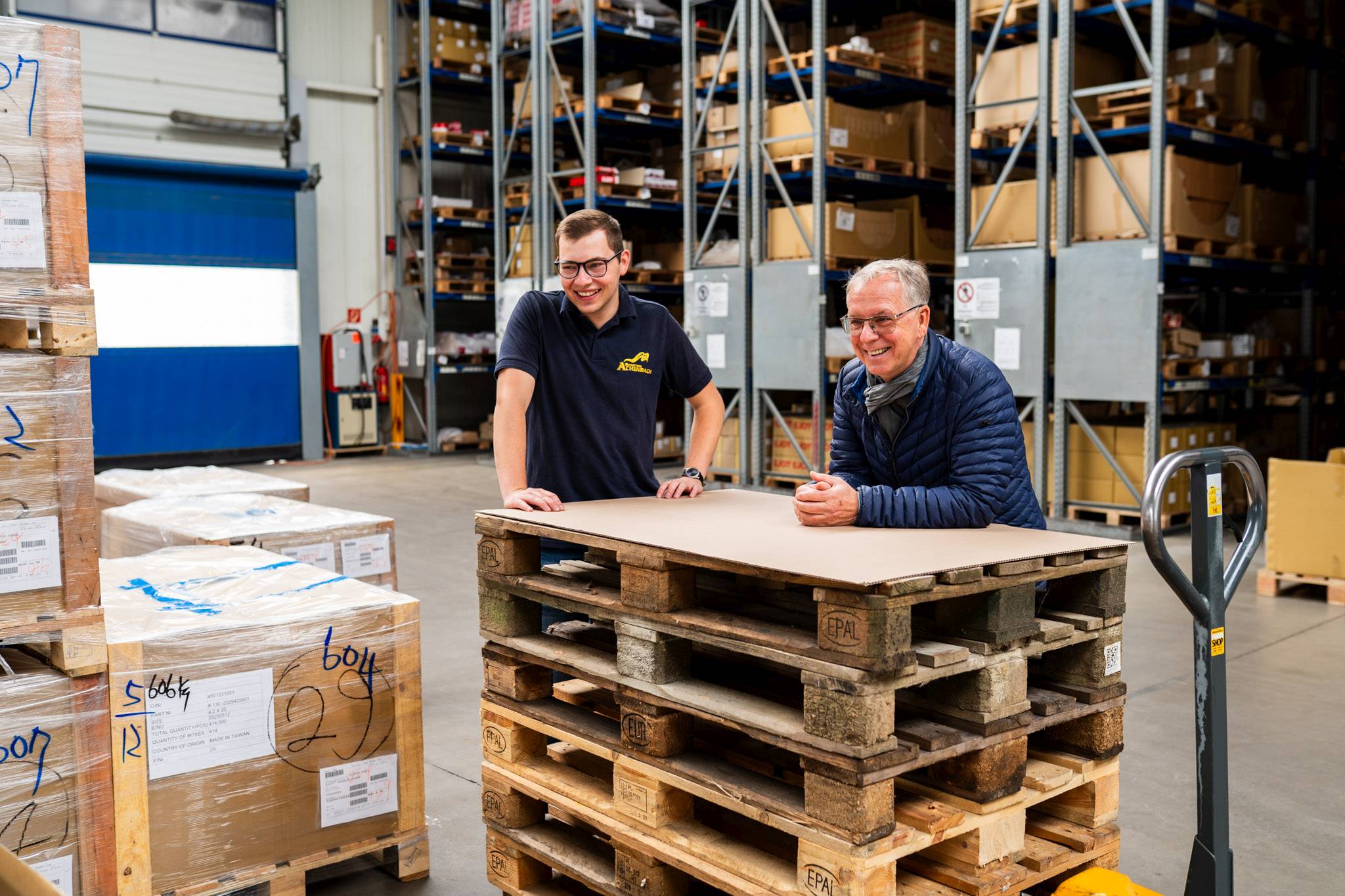 lagerhalle.jpg Zwei Mitarbeiter im Lager von Achenbach im Gespräch an einer Palette – persönliches Miteinander im Team