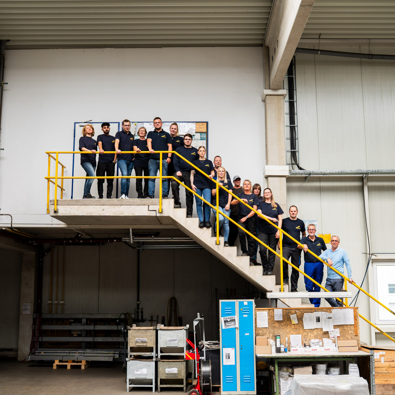 Team Achenbach steht auf der Treppe in der Lagerhalle