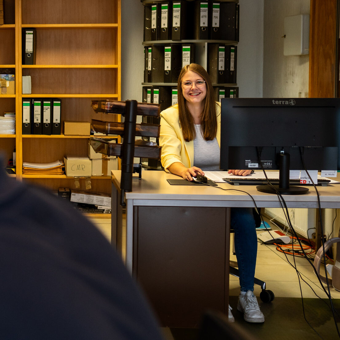 Mitarbeiterin der Spedition Achenbach am Schreibtisch mit Kollegin im Hintergrund