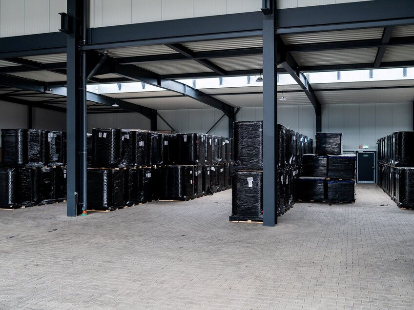 Große Lagerhalle mit vielen auf Paletten gestapelten, schwarz folierten Waren unter einem Stahlträgerdach.